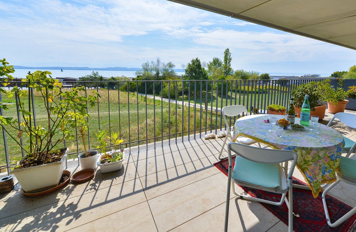 Une terrasse donnant sur un espace vert avec le lac de Neuchâtel en fond, à une centaine de mètres au sud.